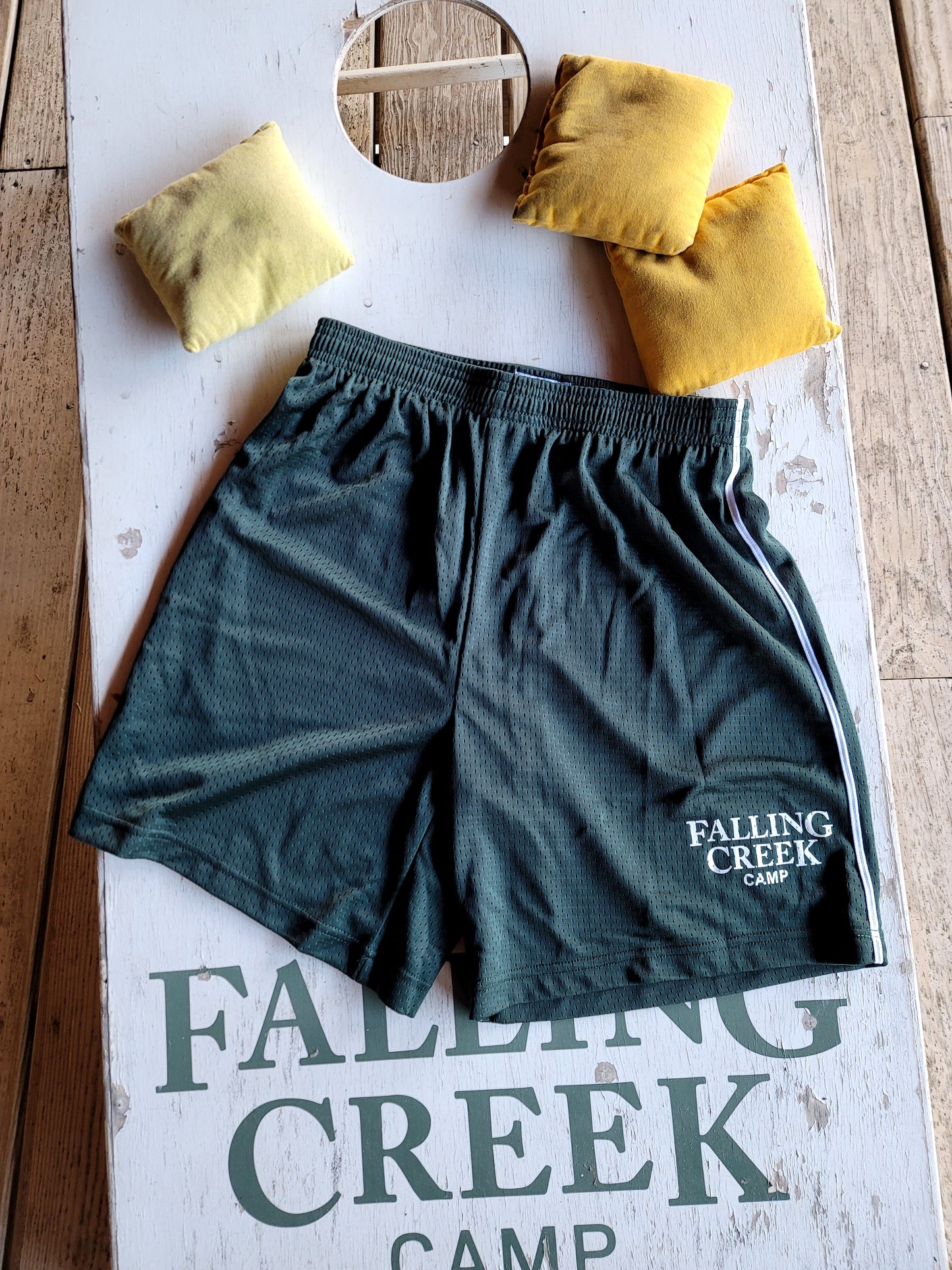 Green Athletic Training Shorts with White Stripe and Falling Creek Camp Logo on Left Leg. Pictured on a cornhole board.